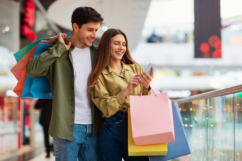 man and woman holding shopping bags looking at a phone together
