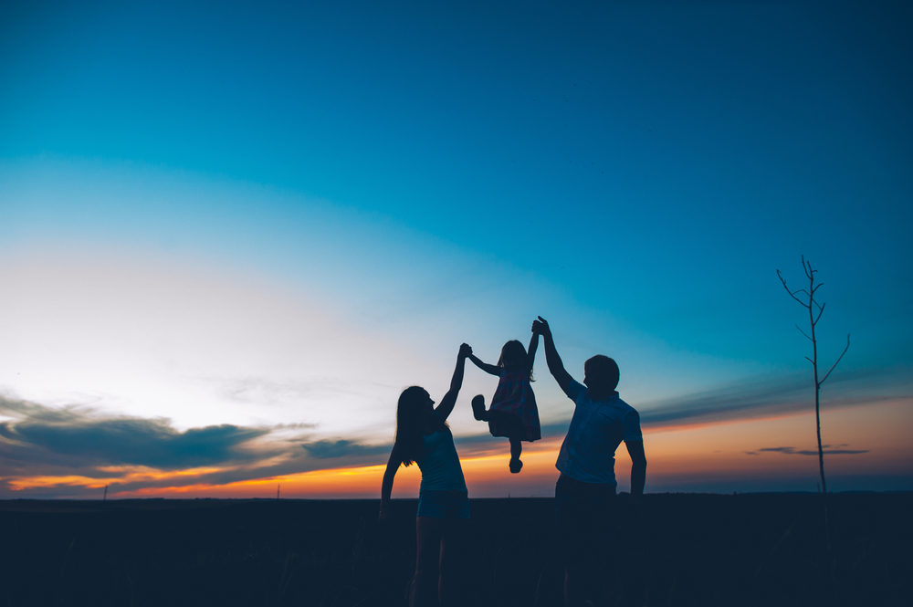 parents holding their child up during a sunset