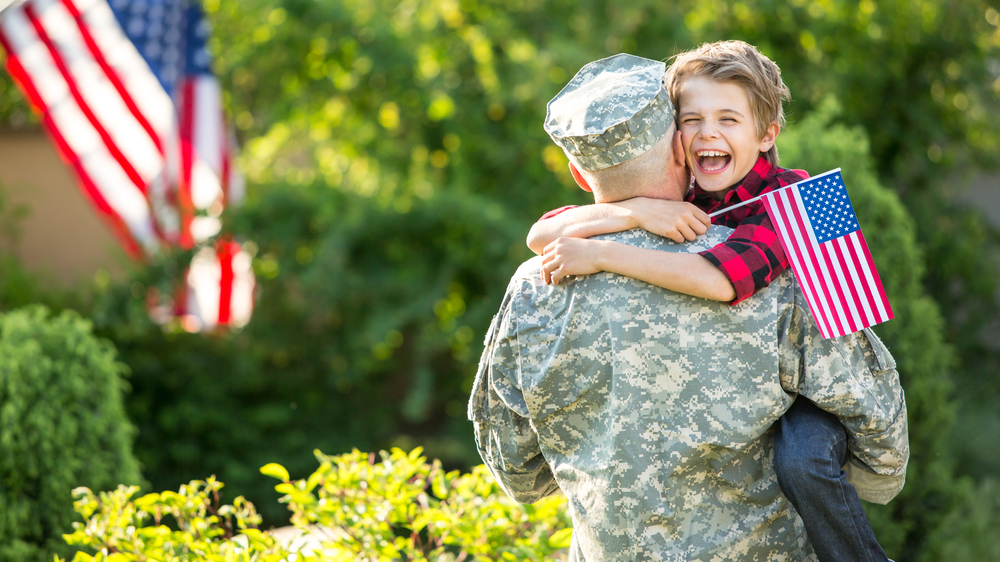 Military serviceman hugging son holding American Flag