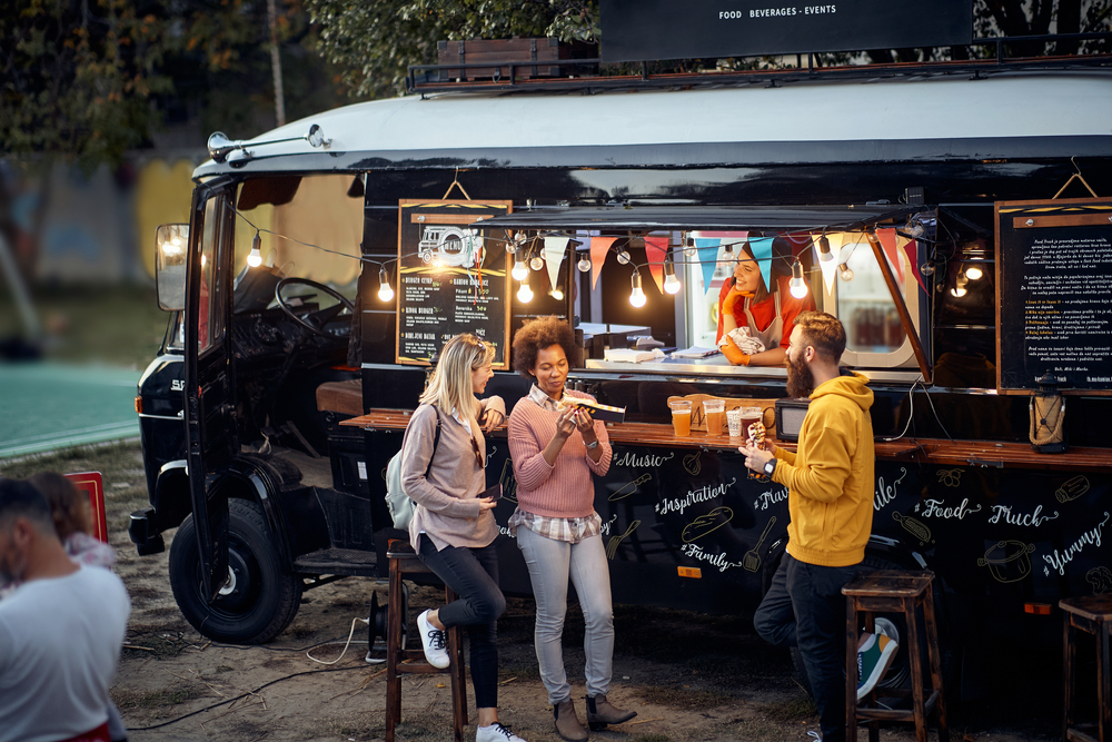 multiple people standing outside a food truck with lights above them