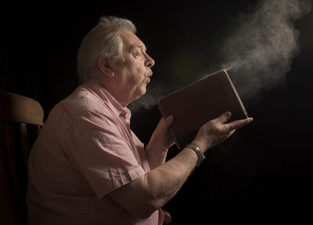 elderly man blowing dust from a book