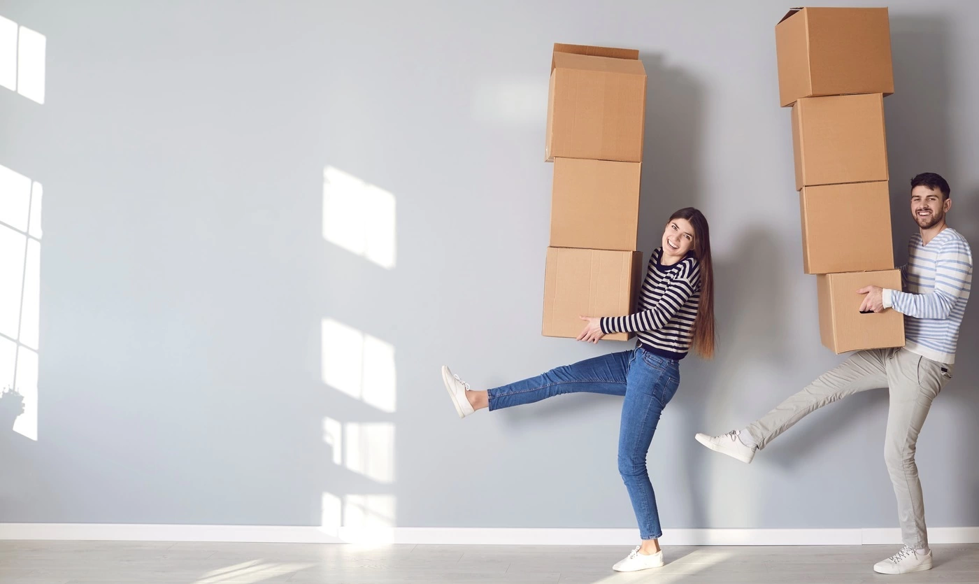 A happy couple having fun striking playful leg-kicking poses while carrying cardboard boxes.